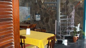 Un comedor con una mesa y sillas amarillas, una pared de piedra, un mapa en la pared y una escalera con barandilla de metal.
