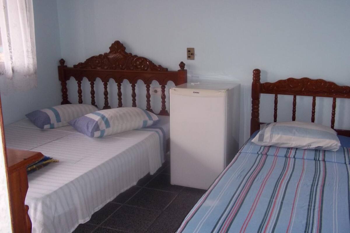 A bedroom with two beds, a small refrigerator, and a wooden headboard.
