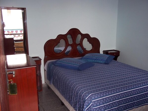 Un dormitorio con una cama de madera, una mesita de noche, un aparador y un espejo.