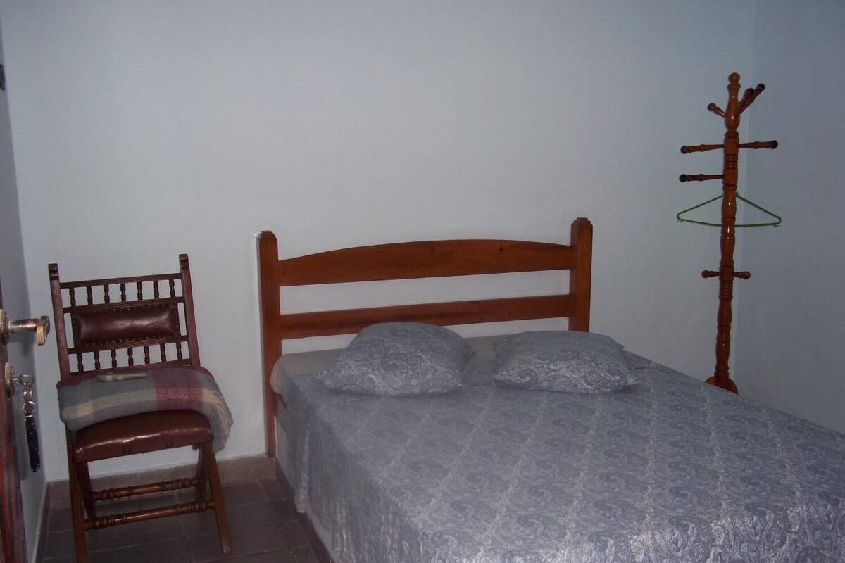 A bedroom with a wooden bed, a chair, and a coat rack.