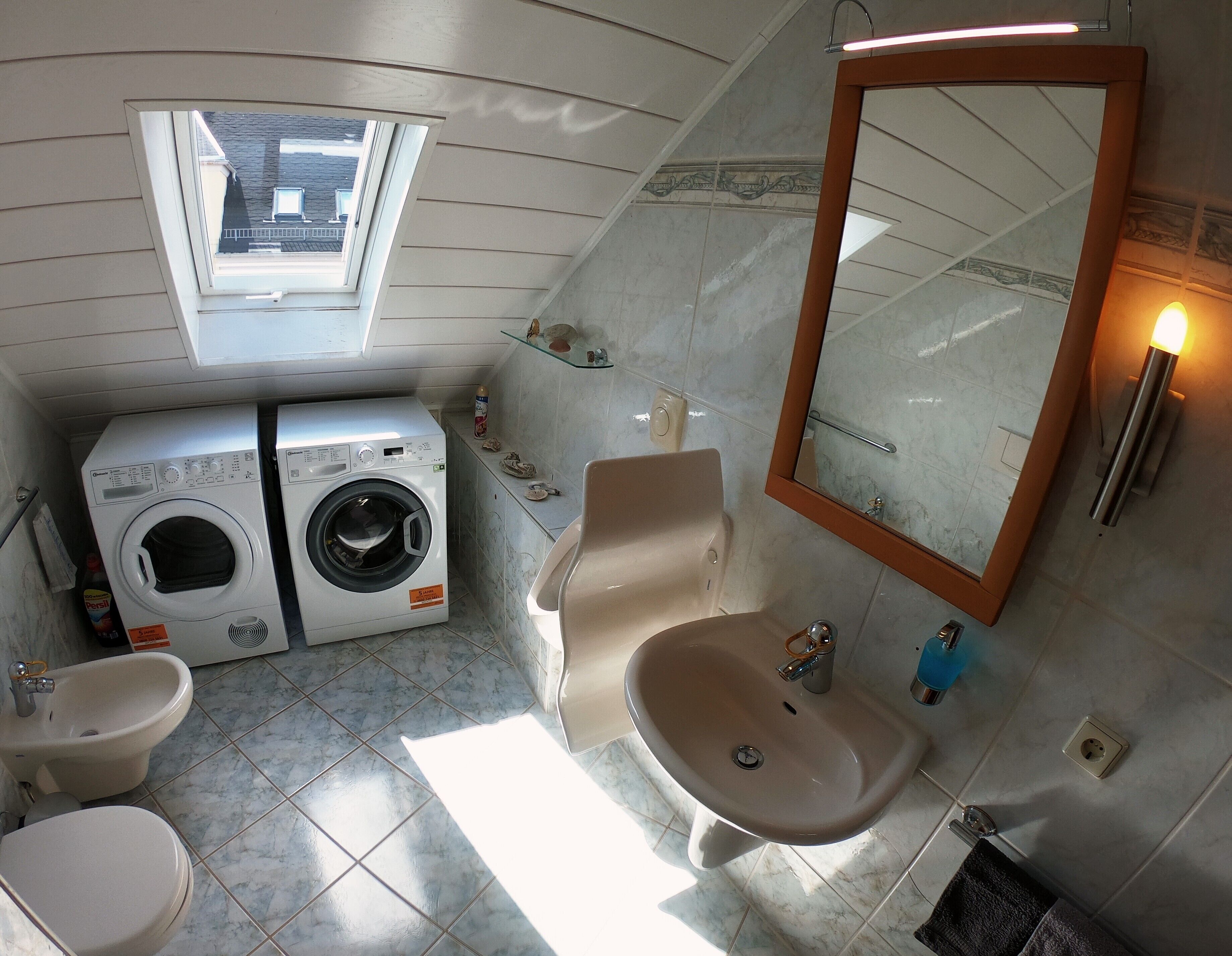 Une petite salle de bain avec un puits de lumière, deux machines à laver, un lavabo et un miroir.