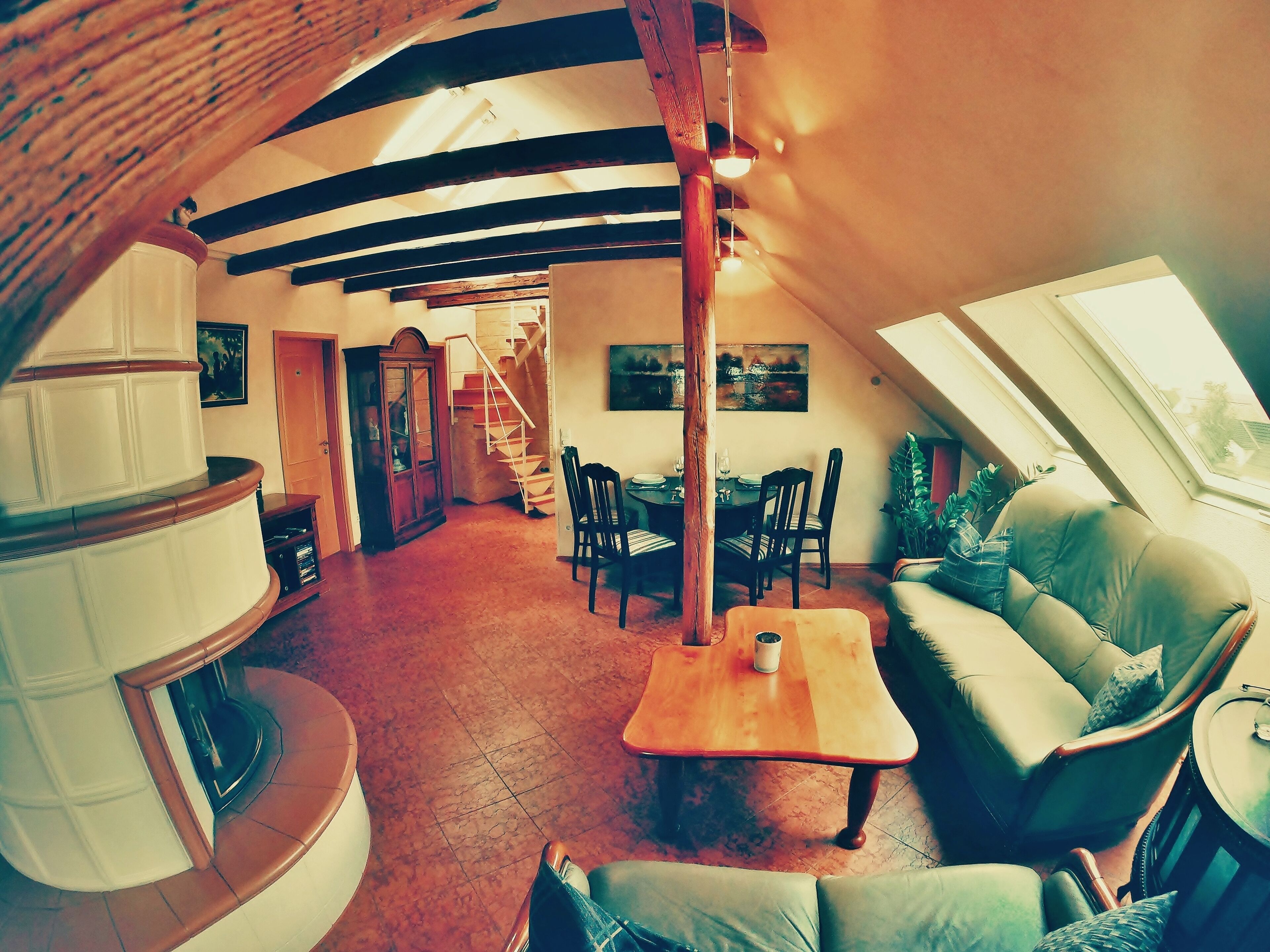 Een ruime loft met een hoge plafond, zichtbare balken, een eethoek met een houten tafel en stoelen, een bank, en een trap naar een hoger niveau.