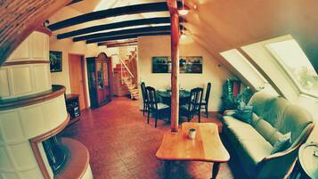 Een ruime loft met een hoge plafond, zichtbare balken, een eethoek met een houten tafel en stoelen, een bank, en een trap naar een hoger niveau.