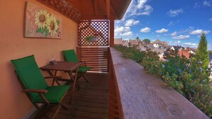 A balcony with wooden flooring, green chairs, a wooden table, and a sunflower painting on the wall.