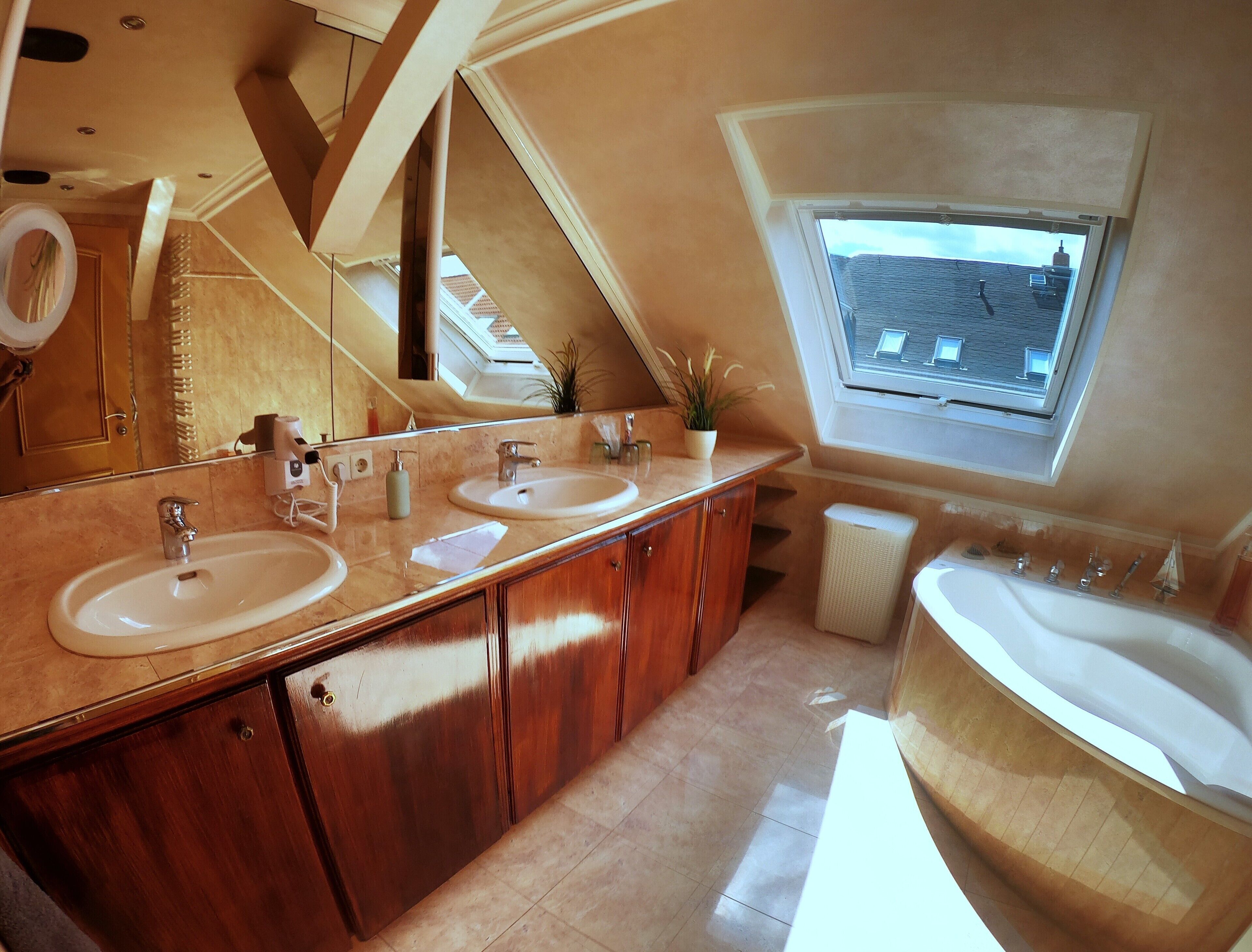 Un bagno moderno con due lavabi, uno specchio grande, armadietti in legno e un lucernario.
