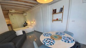 A modern living room with a sofa, a round dining table with chairs, a bed, and a bookshelf.