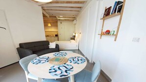 A modern living room with a round table, light blue chairs, a dark sofa, and a kitchen in the background.