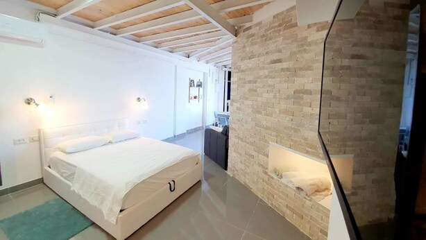 A bedroom with a bed, a brick wall, and a wooden ceiling.