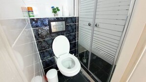 A modern bathroom with a toilet, a hand dryer, and a small potted plant.