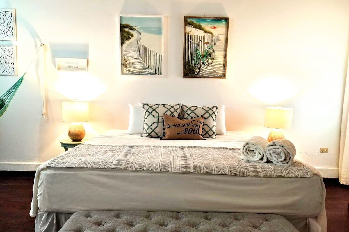 A neatly arranged bedroom with a bed, two pillows, a bedside lamp, and a framed artwork on the wall.