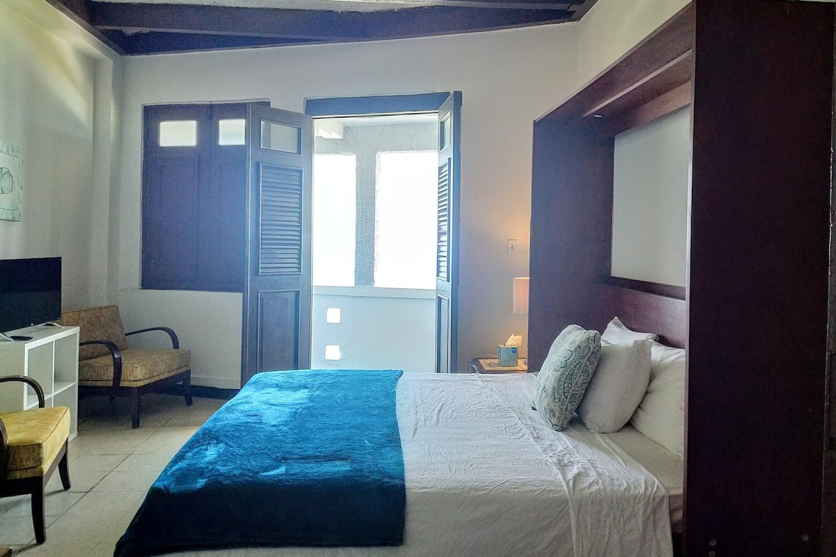 A bedroom with a bed, a chair, a desk, and a window.