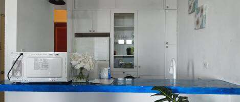 A kitchen with white cabinets, a microwave, a sink, and a plant.