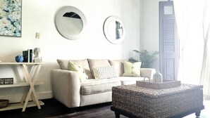 Ein Wohnzimmer mit einer Couch, einem Couchtisch, einem Beistelltisch mit Büchern und zwei Wandspiegeln.