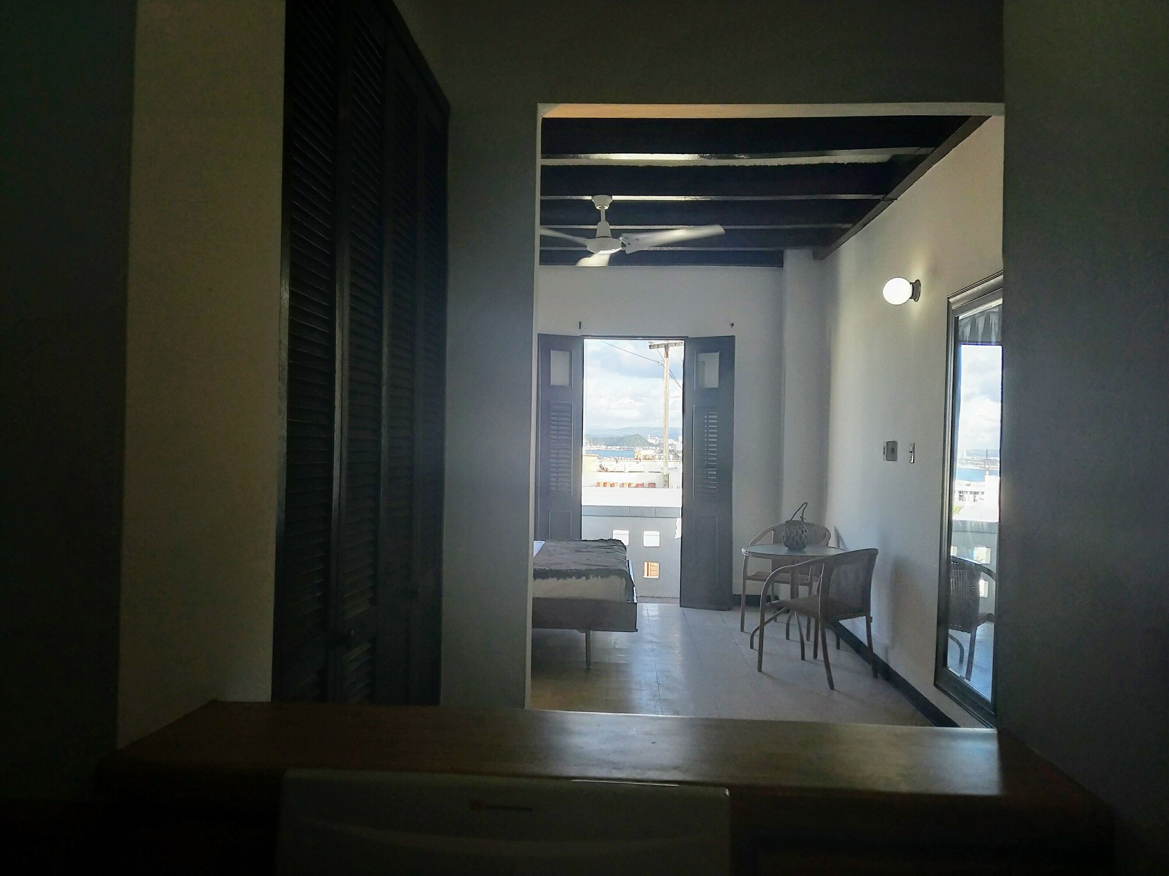 A narrow hallway leading to a balcony with a table and chairs, a ceiling fan, and a view of the cityscape.