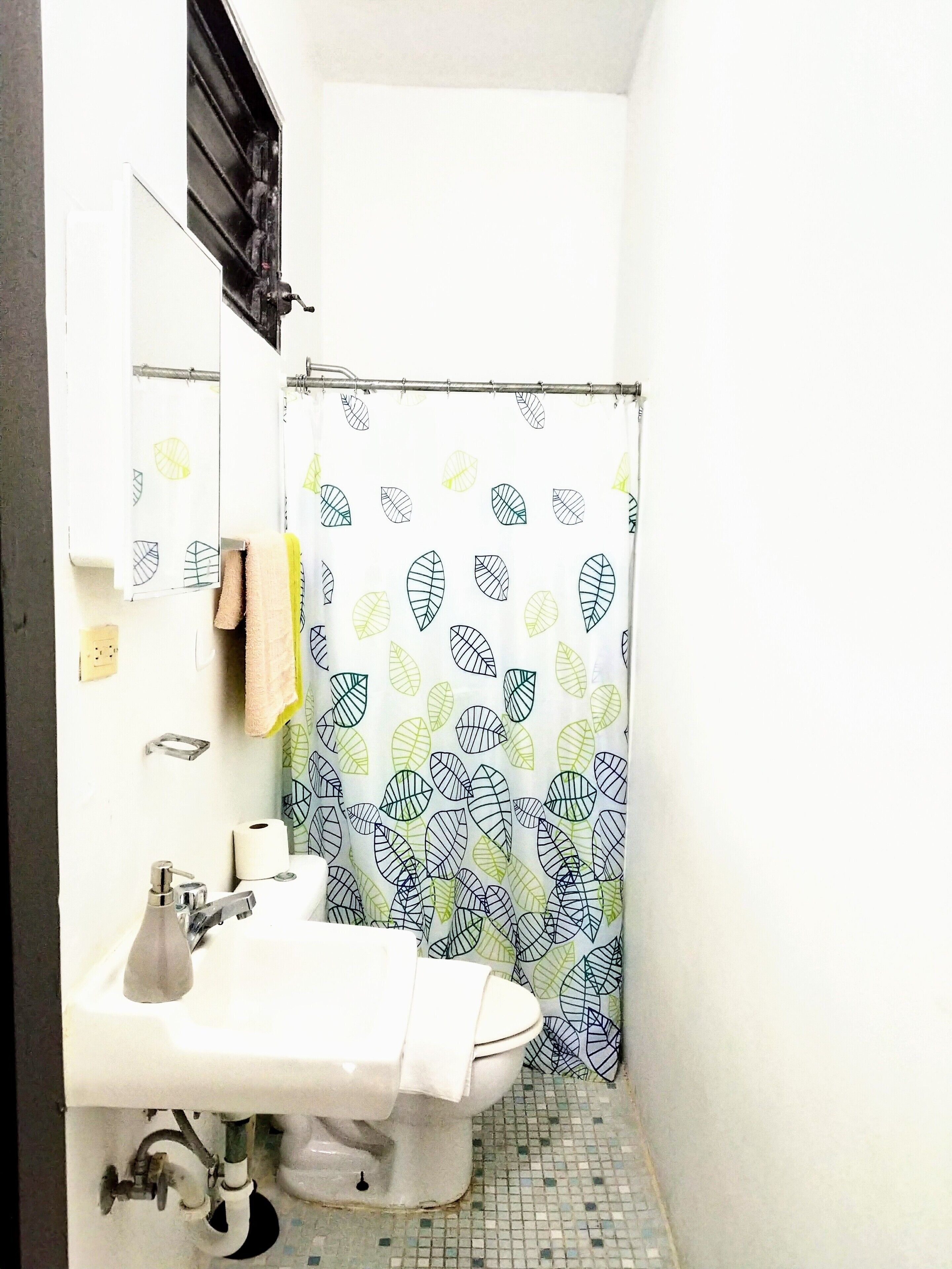 Ein kleines Badezimmer mit einem weißen Waschbecken, einer Toilette und einer Duschvorhang mit Blättermotiv.