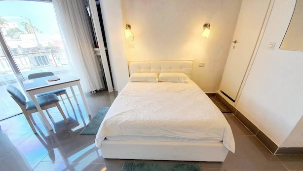 A modern hotel room with a large bed, a desk with a chair, and a view of the outside. - Agas Holiday Apartments Gefen Boutique (Tiberias)