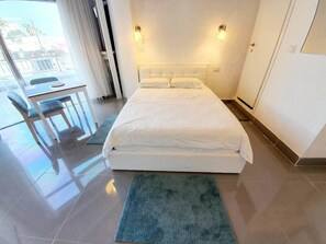 A modern hotel room with a large bed, a desk with a chair, and a view of the outside. - Agas Holiday Apartments Gefen Boutique (Tiberias)