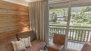 A cozy room with a brown leather sofa, a wooden coffee table, and a view of a green landscape through large windows. - Rosentalerhof Hotel & Apartments (Saalbach-Hinterglemm)