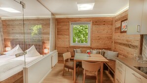 A cozy cabin-style room with a bed, a dining table, and a window overlooking greenery. - Rosentalerhof Hotel & Apartments (Saalbach-Hinterglemm)