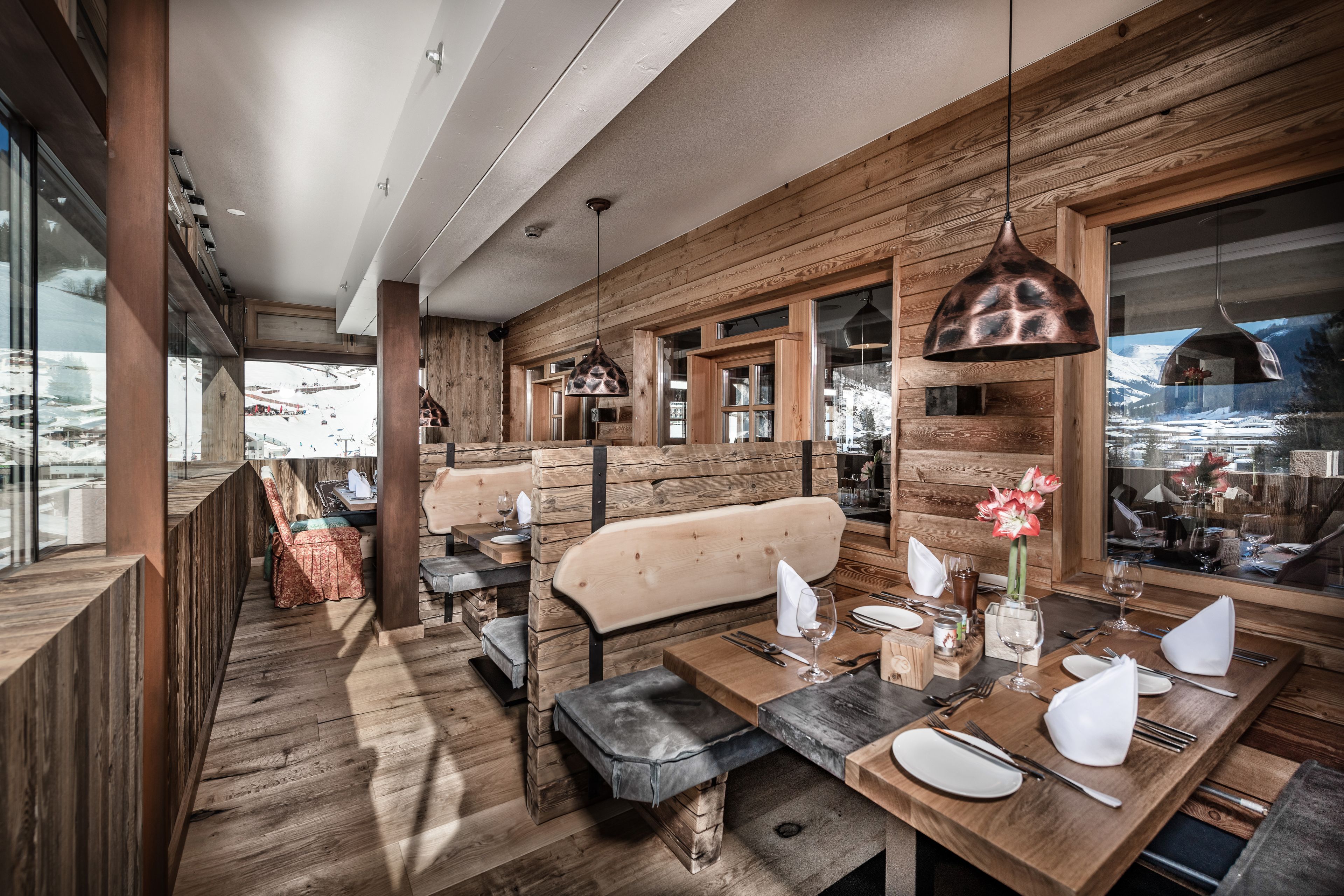 A restaurant with wooden walls and a view of a snowy landscape. Tables are set with white tablecloths and silverware.