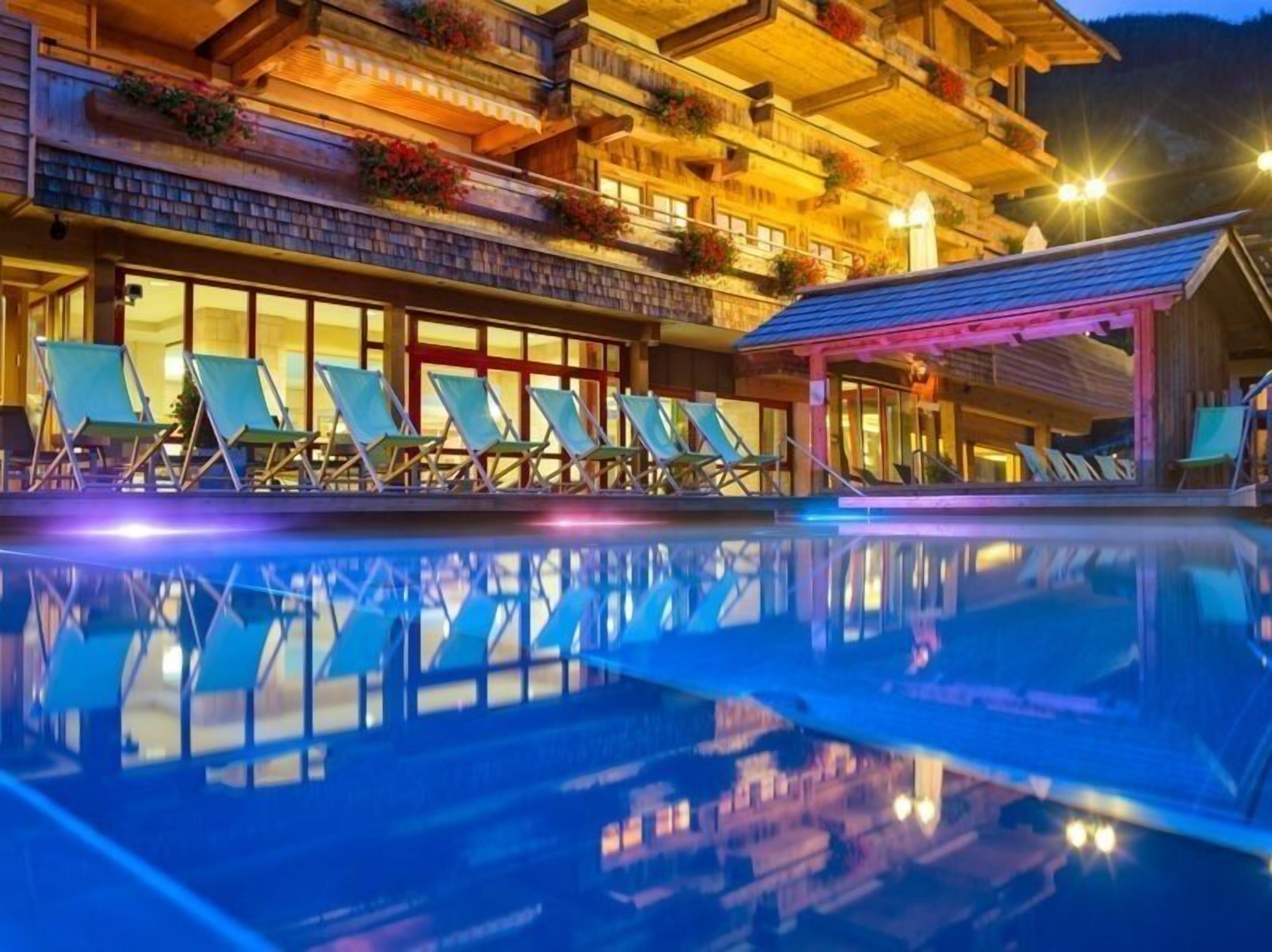 A hotel with a pool, lounge chairs, and a building with balconies decorated with flowers.