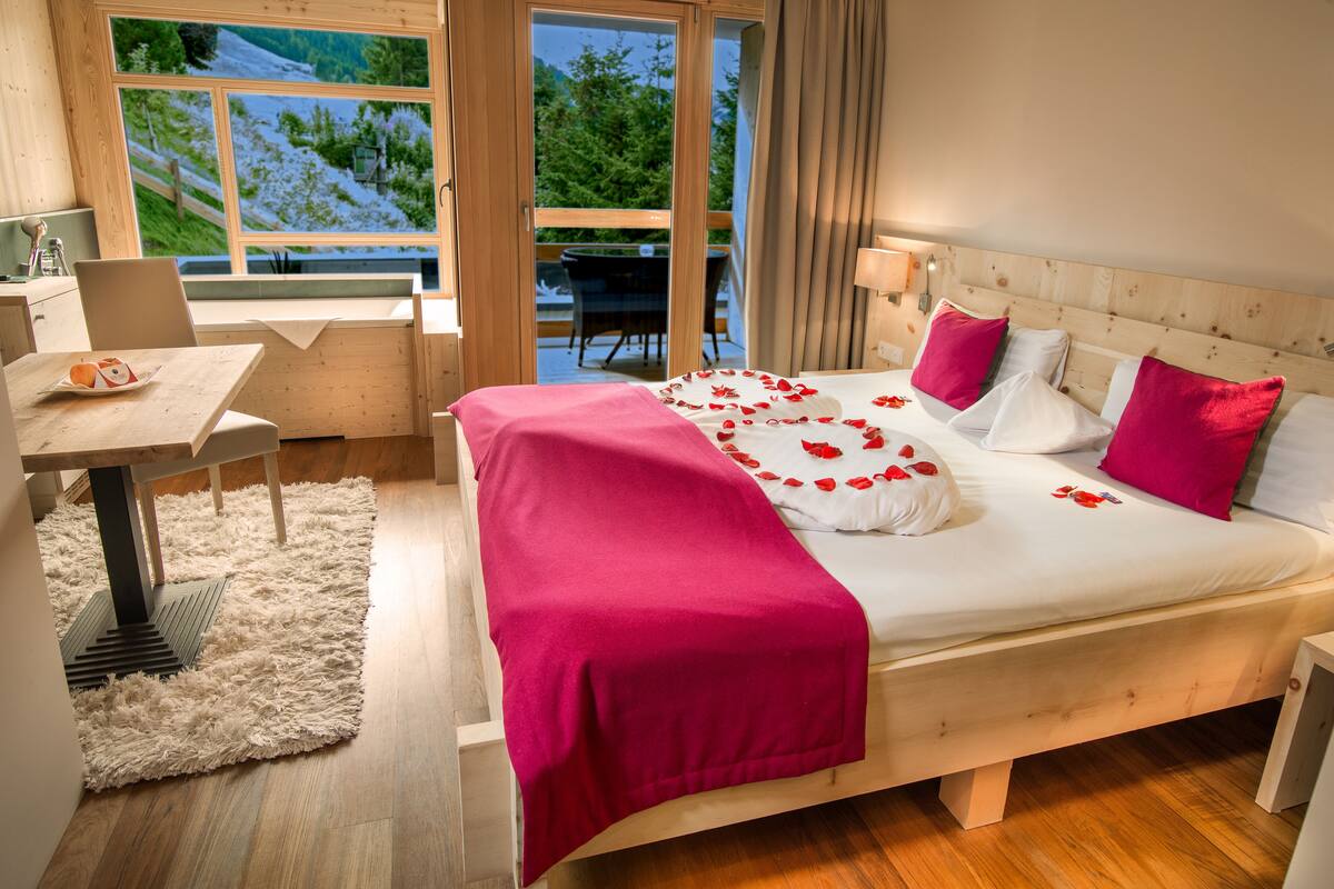 Une chambre avec un lit en bois, un bureau et une vue sur une forêt, visible à travers de grandes fenêtres.