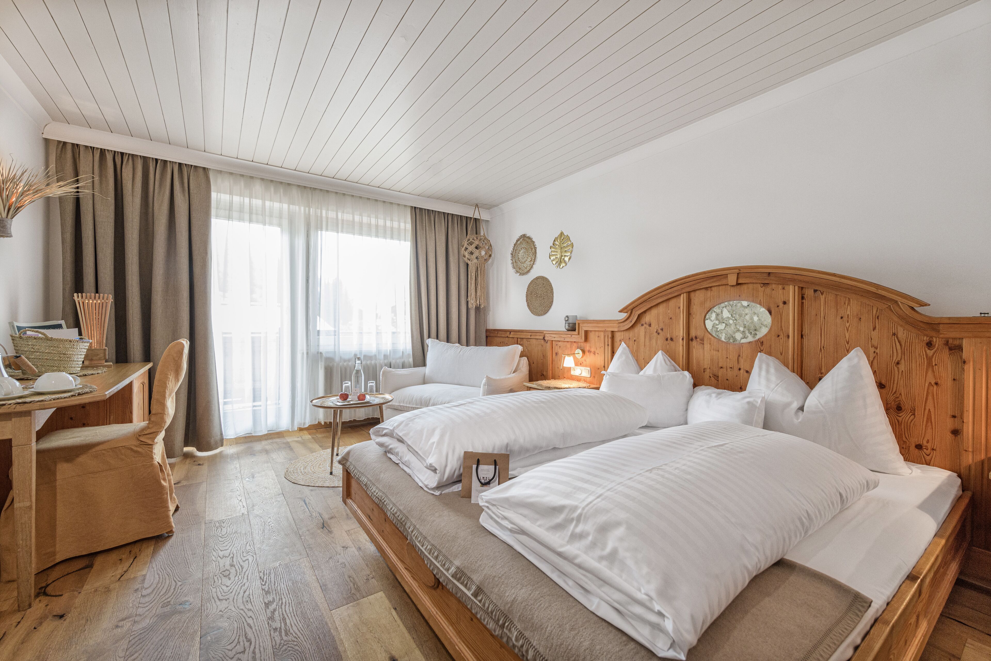 Ein Hotelzimmer mit zwei Betten, einem Holzkopfstück, einem kleinen Tisch, einem Stuhl und einem Vorhangfenster.