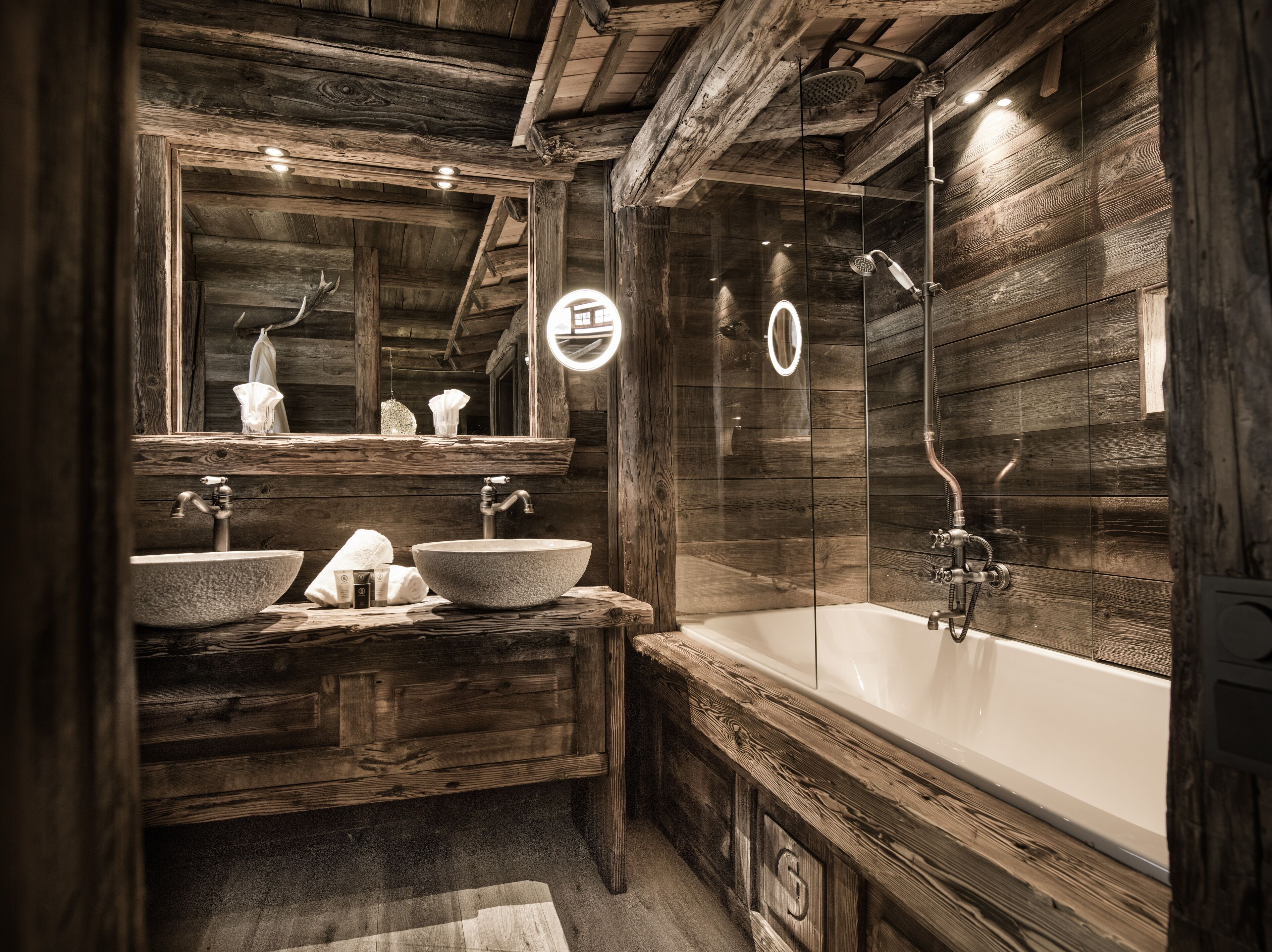 Ein rustikales Badezimmer aus Holz mit einer großen Badewanne, zwei Waschbecken und einem Spiegel.