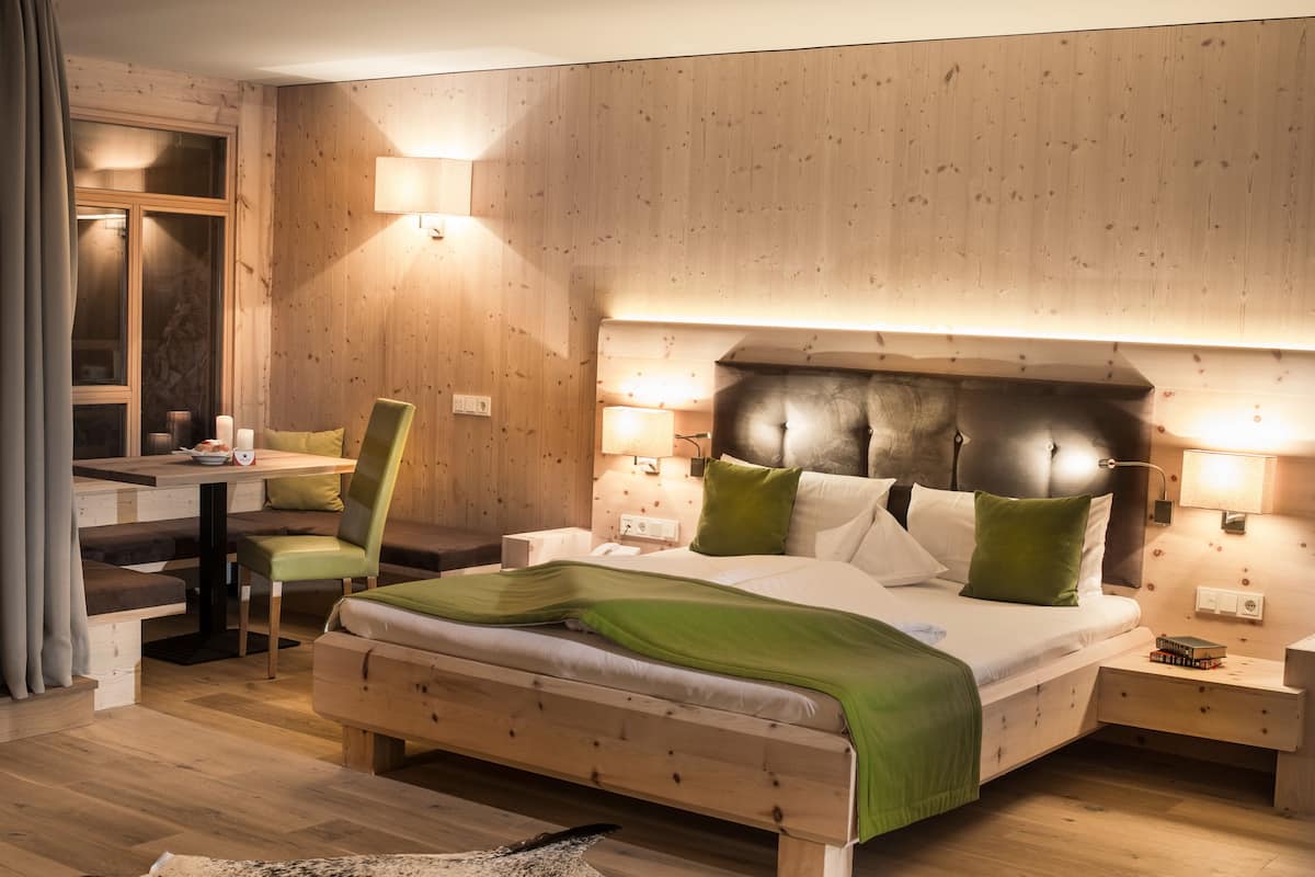 Une chambre moderne avec une tête de lit en bois, une couvre-lit verte et un coin repas comprenant une chaise et une table.