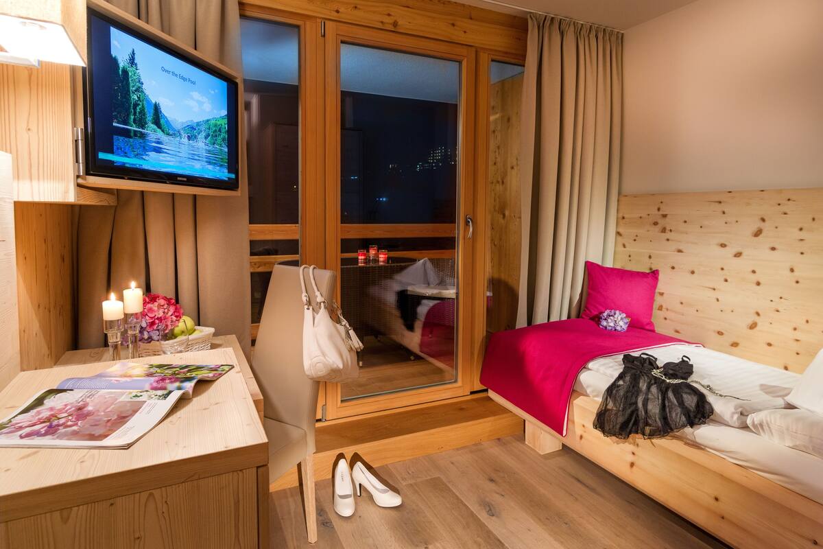 Une chambre à coucher avec un lit, une télévision, un bureau en bois et une fenêtre avec des rideaux.