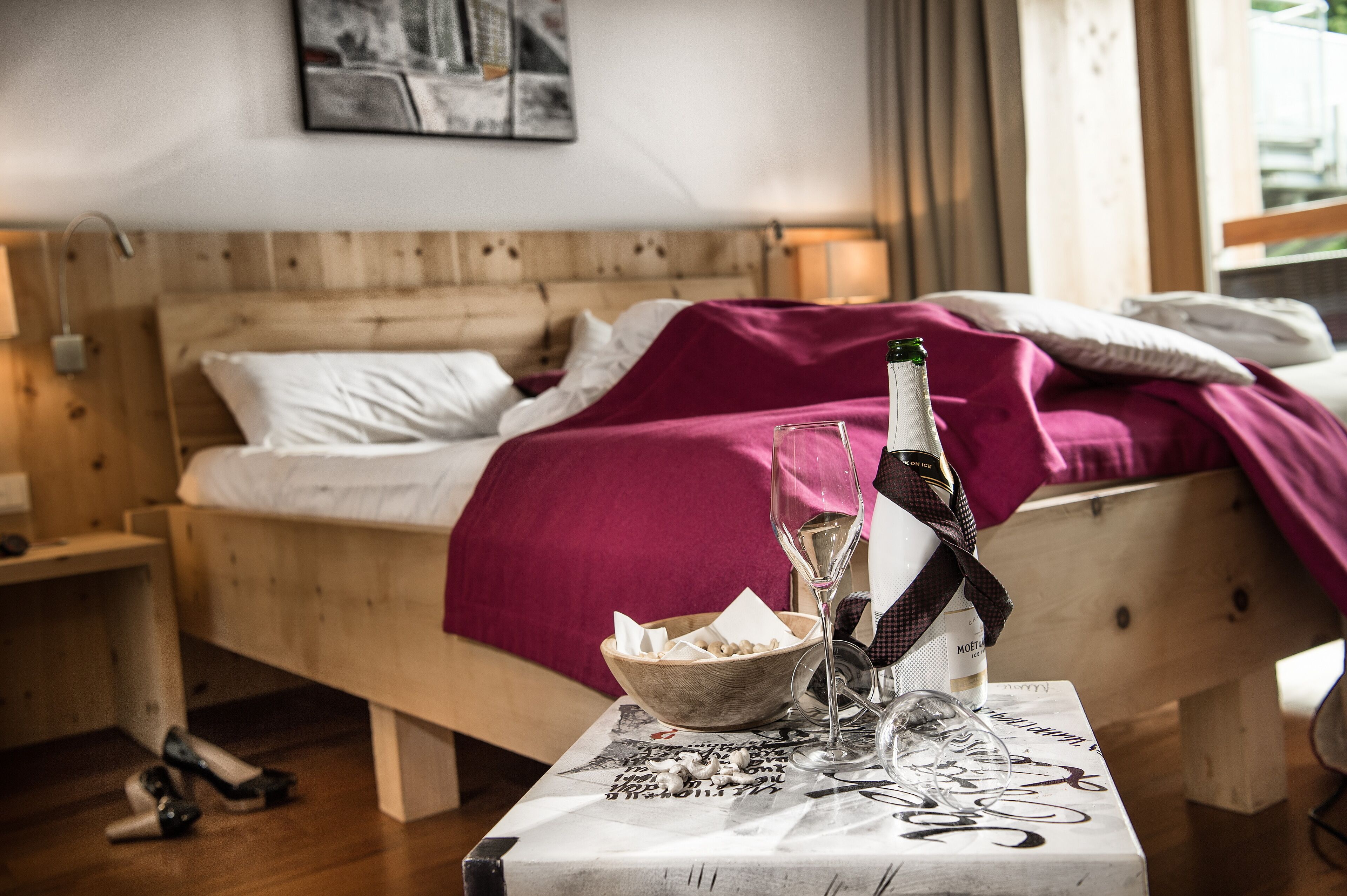 Una cama de madera con una manta morada, una botella de vino y un cuenco con aperitivos sobre una mesa con un periódico.