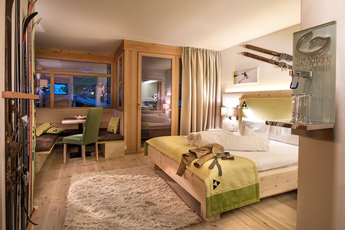 Une chambre d’hôtel équipée d’un lit, d’un bureau, d’une chaise, d’un porte-skis et d’une fenêtre donnant sur une piste de ski.