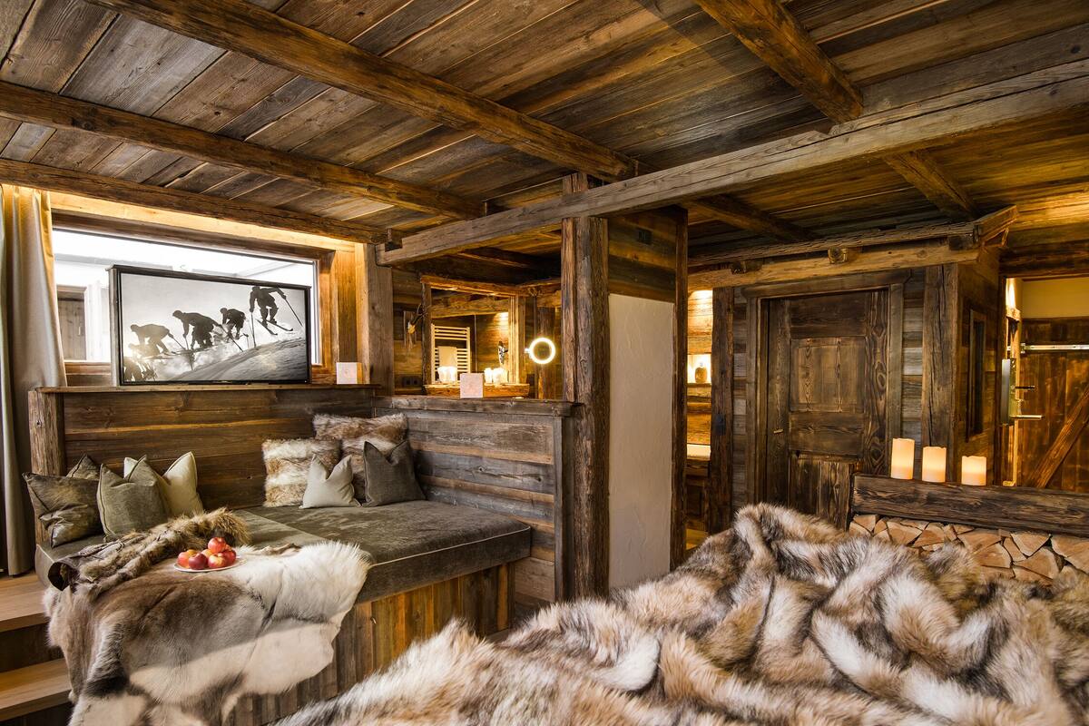 L'intérieur d'un chalet rustique, avec un banc en bois, un plaid en fourrure et des bougies.