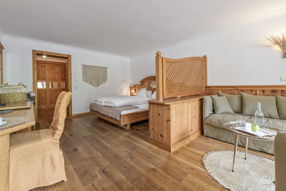 Une pièce chaleureuse avec un lit en bois, un canapé en bois, une petite table avec un plateau en verre et une chaise.