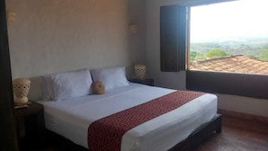A bedroom with a large bed, a window with a view, and a nightstand with a lamp. - La Loma Hotel Barichara (Barichara)