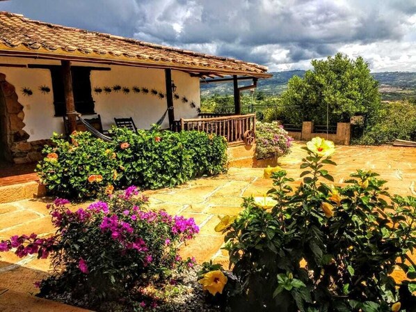 Une villa dotée d’un toit en tuiles, d’une terrasse en pierre et d’un jardin où poussent différentes variétés de fleurs.