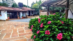 A courtyard with a stone pathway, a covered seating area, and a building with a tiled roof. - La Loma Hotel Barichara (Barichara)
