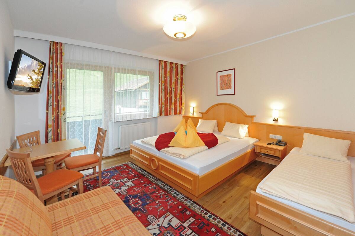 Una habitación de hotel con cama, mesita de noche, lámpara y televisor en la pared.