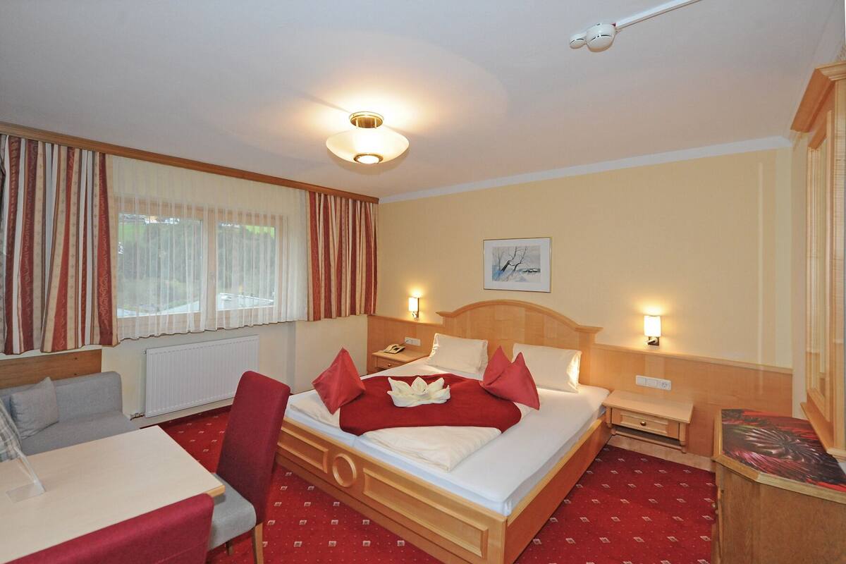 Habitación de hotel con cama, escritorio, silla, mesita de noche y ventana con cortinas.