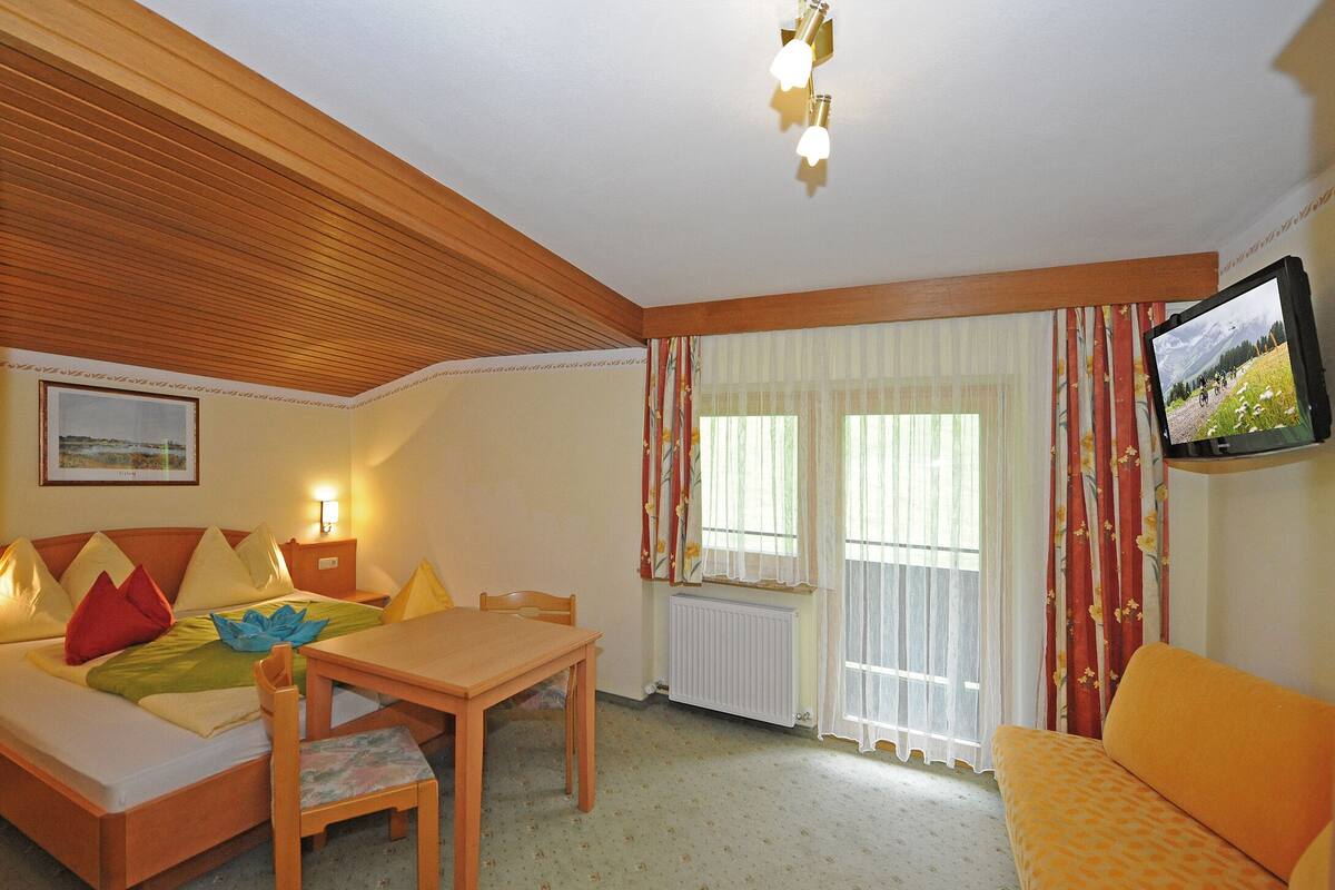 Una habitación acogedora con una cama, una mesa de madera, un sofá y un televisor.