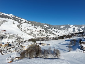 En snedækket bjerglandsby med spredte bygninger, en skibakke og en klar blå himmel.