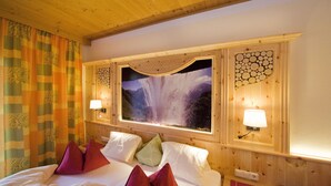Habitación de hotel con una cama grande, dos lámparas de noche, una ventana con vistas a una cascada y techo de madera.