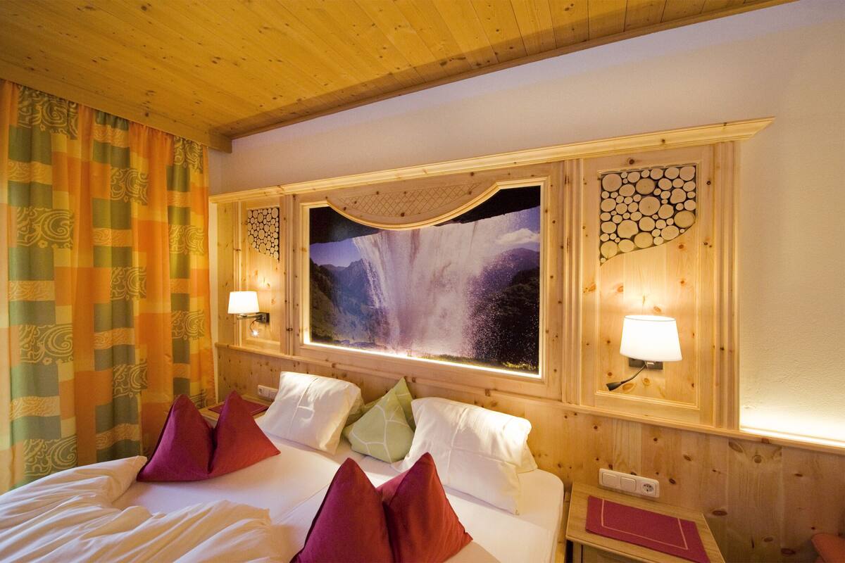 Habitación de hotel con una cama grande, dos lámparas de noche, una ventana con vistas a una cascada y techo de madera.