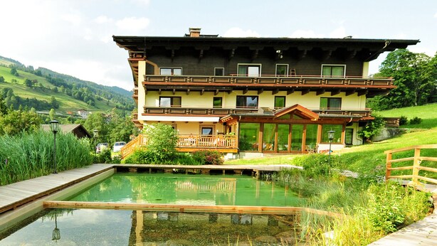 Un chalet de dos plantas con piscina, rodeado de exuberante vegetación y colinas.