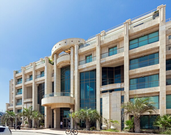 A modern building with multiple floors, large windows, and a curved entrance. - Lagoon Amazing water front 3 (Herzliya)