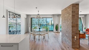 A modern living room with a dining area, large windows with a city view, and a brick accent wall. - Lagoon Amazing water front 3 (Herzliya)