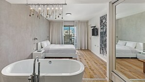 A modern bedroom with a large bathtub, a bed, and a city view through the window. - Lagoon Amazing water front 3 (Herzliya)