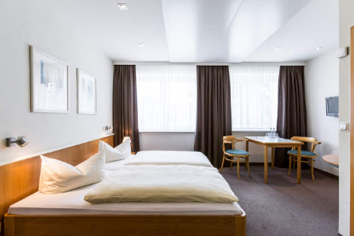 A hotel room with a bed, two chairs, a small table, and a window with curtains.