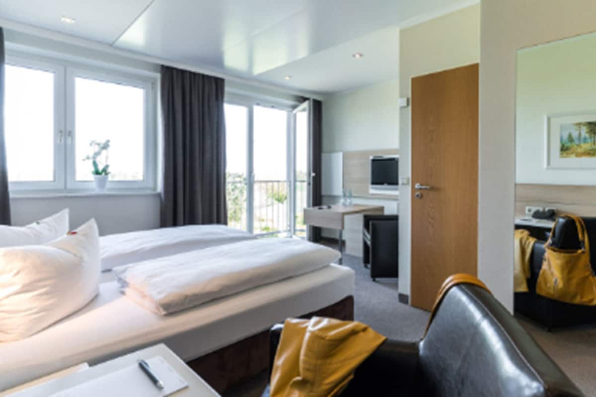 A hotel room with two beds, a desk, a chair, a TV, and a door leading to a balcony.