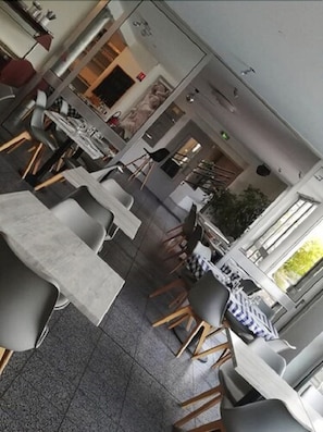 A spacious dining area with high tables and chairs, a large plant, and a view of the outdoors. - Hôtel la clé (Saint-Andre-de-Sangonis)